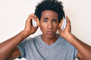 Afro saçlı, kulaklık takan, kuşkucu ve sinirli, sorun yüzünden üzgün olan yakışıklı Afro-Amerikan bir adam. negatif kişi. 
