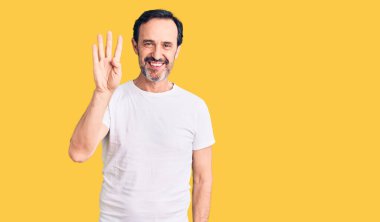 Orta yaşlı yakışıklı bir adam gündelik tişört giyer ve parmaklarıyla dört numarayı gösterirken kendinden emin ve mutlu bir şekilde gülümserdi.. 