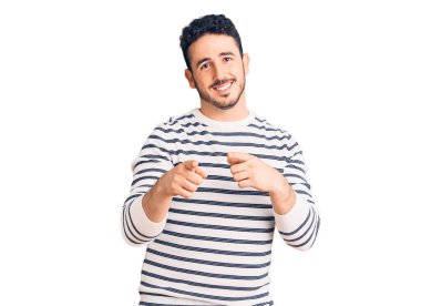 Günlük kıyafetler giyen genç İspanyol adam mutlu ve komik yüzüyle kamerayı işaret ediyor. iyi enerji ve titreşimler. 