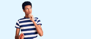 Genç Afrikalı Amerikalı bir adam elinde süpermarket sepetini tutarken ciddi bir yüz ifadesiyle eli çenesinde soru sorarken, kafa karıştırıcı bir fikir hakkında düşünceli. 