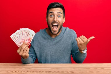 Yakışıklı, israil şekelleri tutan, ağzı açık gülümseyen ve gülümseyen bir adam. 