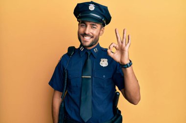 Yakışıklı, polis üniforması giyen, gülümseyen ve el ve parmaklarıyla imza atan İspanyol. başarılı ifade. 