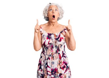 Kıdemli gri saçlı kadın, gündelik kıyafetler giyip şaşkın şaşkın yukarı bakıyor, parmaklarıyla işaret ediyor ve kollarını kaldırıyordu.. 