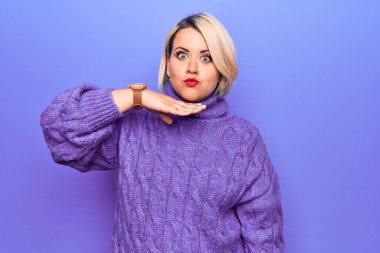 Güzel sarışın, iri yarı, balıkçı yaka kazak giyen, mor arka planda boğazını bıçak niyetine kesen, saldırganlığı şiddetle tehdit eden bir kadın.