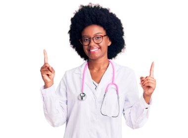 Doktor önlüğü ve steteskop giyen genç Afro-Amerikan kadın parmaklarıyla farklı yönleri gösteren kendine güvenle gülümsüyor. reklam için kopyalama alanı 