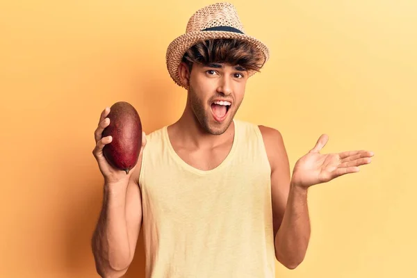 Young Hispanic Man Wearing Hat Holding Mango Celebrating Achievement Happy — Stock Photo, Image