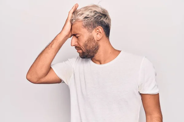 Young handsome blond man wearing casual t-shirt standing over isolated white background surprised with hand on head for mistake, remember error. Forgot, bad memory concept.