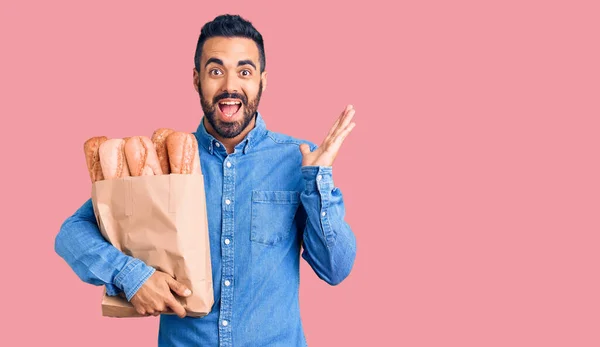 Jovem Hispânico Homem Segurando Saco Com Pão Celebrando Vitória Com — Fotografia de Stock