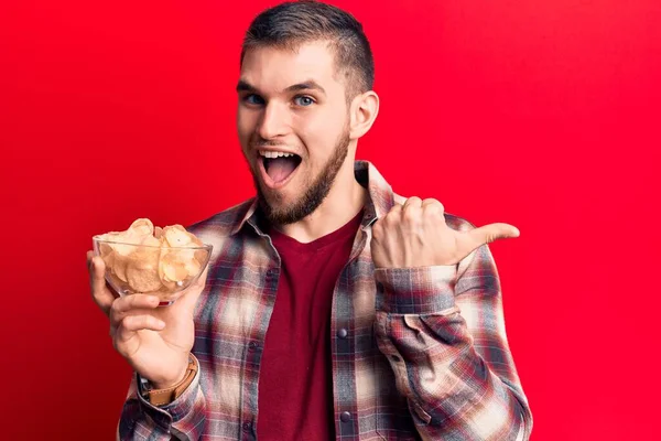 Joven Hombre Guapo Sosteniendo Tazón Con Papas Fritas Apuntando Pulgar — Foto de Stock