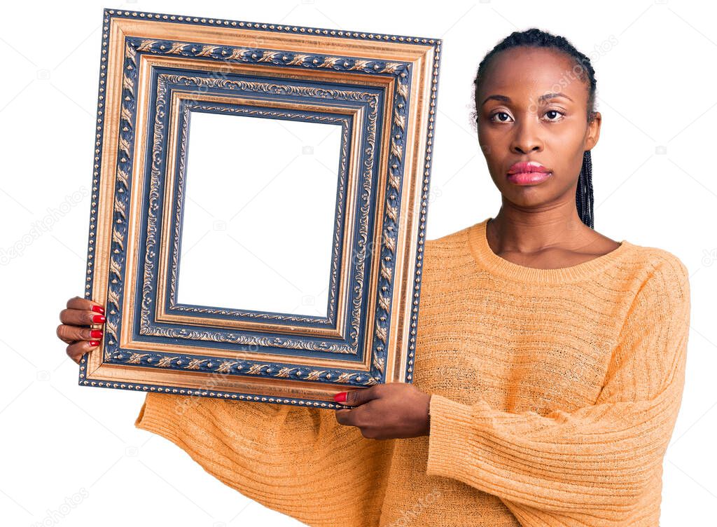 Young african american woman holding empty frame thinking attitude and sober expression looking self confident 