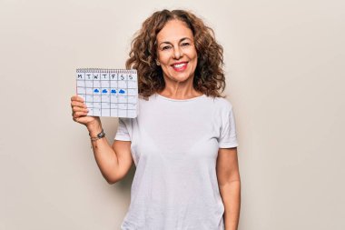 Orta yaşlı güzel bir kadın, elinde iklim takvimi tutarken bulutlu ve yağmurlu havanın pozitif ve mutlu göründüğünü dişlerini gösteren bir gülümsemeyle ayakta durduğunu ve gülümsediğini gösteriyor.