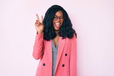 İş ceketi giyen, gözlüklü, gülümseyen, kameraya göz kırpan ve zafer işareti yapan güzel Afrikalı kadın. İki numara.. 