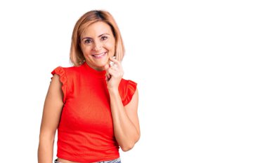 Sıradan kıyafetler giyen genç sarışın kadın kameraya özgüvenli bakıyor kollarını kavuşturup gülümseyerek ve çenesini kaldırarak. Olumlu düşünmek. 