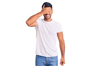 Gündelik kıyafetler giyen, gülümseyen ve gülümseyen genç latin adam şaşırmak için gözlerini kapatıyor. kör kavram. 