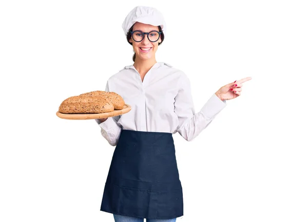 Hermosa Morena Joven Con Uniforme Panadero Sosteniendo Pan Casero Sonriendo — Foto de Stock