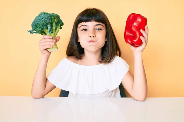 一个年轻的小女孩 带着蓬松的花椰菜和红辣椒 脸上带着滑稽的表情 嘴被空气吹胀 — 图库照片