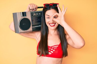 Bikini giyen, elinde teyp çalan, gülümseyen, el pençe divan duran güzel beyaz bir kadın. 