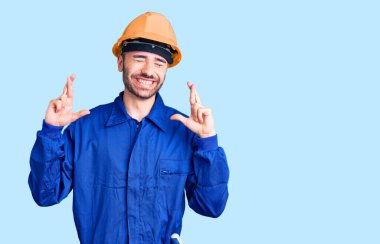 İşçi üniforması giyen genç İspanyol adam umut ve gözlerin kapalı gülümseyerek bana işaret ediyor. Şans ve batıl inançlar. 