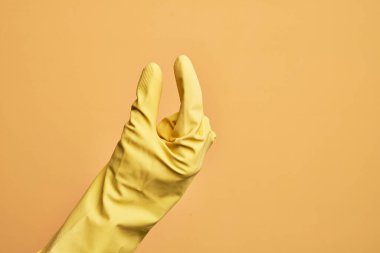 İzole edilmiş sarı arka plan üzerinde temizlik eldiveni olan beyaz bir adamın eli. Görünmez bir şeyi alıp, parmaklarında boşluk gösteren bir nesneyi tutuyor.