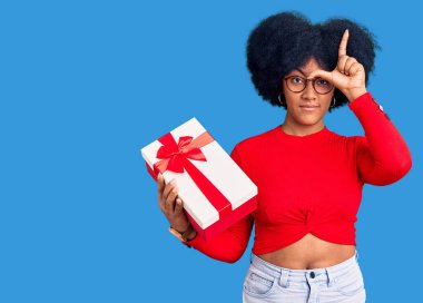 Genç Afro-Amerikalı kız elinde hediyeyle, alnında parmakları olan insanlarla dalga geçiyor. Ezik hareketler yapıyor, alay ediyor ve hakaret ediyor.. 