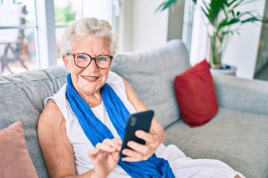 Yaşlı, yaşlı, gri saçlı, gülümseyen, mutlu, akıllı telefon kullanan bir kadın.