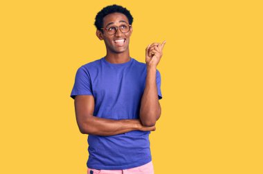 Sıradan kıyafetler giyen ve gözlüklü, yüzünde kocaman bir gülümseme olan, eli ve parmağı kameraya bakan Afrikalı yakışıklı bir adam.. 