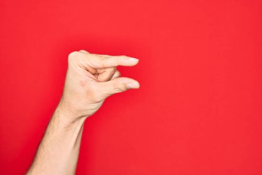 Kafkasyalı genç adam parmaklarını izole edilmiş kırmızı arka plan üzerinde gösteriyor ve görünmez şeyi alıyor, parmakları boşluk gösteren nesneleri tutuyor.