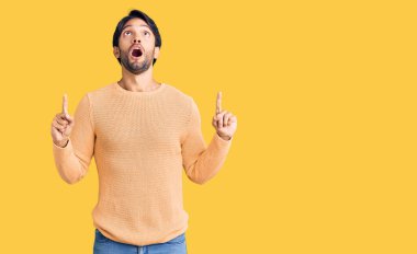 Yakışıklı İspanyol bir adam gündelik süveter giyer. Şaşırır ve şaşırır. Parmaklarıyla işaret eder ve kollarını kaldırır.. 