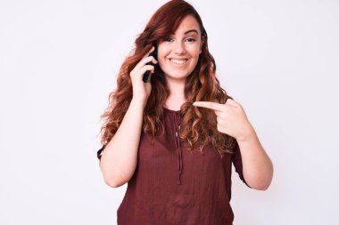 Genç ve güzel bir kadın akıllı telefondan konuşuyor. Kendini mutlu ve gururlu bir şekilde gösteren birini işaret ediyor. 