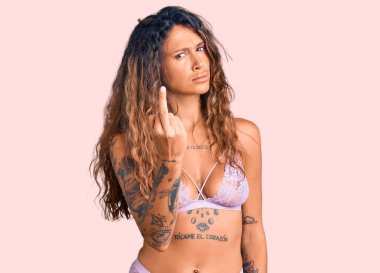 Young hispanic woman with tattoo wearing lingerie showing middle finger, impolite and rude fuck off expression 