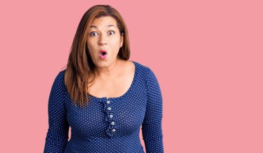 Orta yaşlı, sıradan kıyafetler giyen, ağzı açık, korkmuş, şaşırmış bir Latin kadın. 