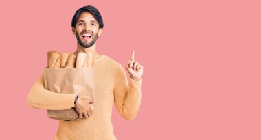 Elinde ekmek torbası olan yakışıklı İspanyol bir adam bir fikre ya da soru işaretine şaşırmış ve mutlu bir yüzle işaret ediyor. 