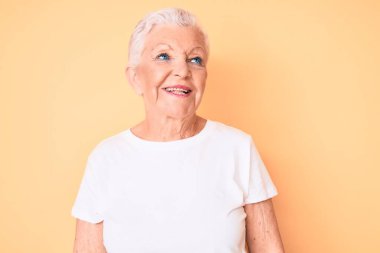 Son sınıf güzeli, mavi gözlü, gri saçlı, sarı arka planda klasik beyaz tişört giyen, yüzünde gülümseme, doğal bir ifade ile bir yana bakan güzel bir kadın. Kendinden emin gülen. 