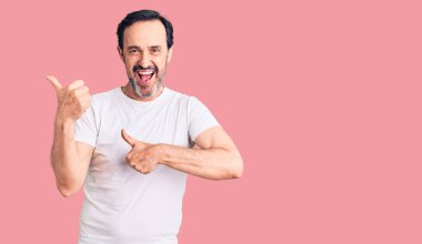 Orta yaşlı, sıradan tişörtler giyen yakışıklı bir adam arka tarafı işaret ediyor. Baş parmakları havada, kendine güveni tam. 