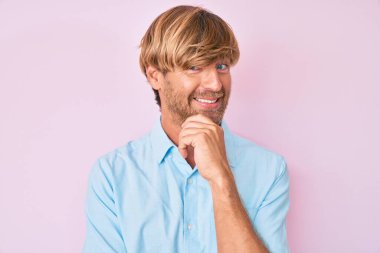 Sıradan kıyafetler giyen genç sarışın adam kameraya kollarını kavuşturmuş ve çenesi üzerinde kendinden emin bir şekilde bakıyor. Olumlu düşünmek. 