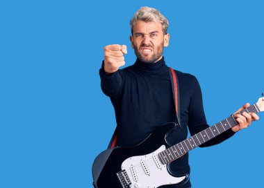 Genç, sarışın ve elektro gitar çalan yakışıklı bir adam öfkeyle bağırıyor, öfkeyle bağırıyor ve el kaldırıyor. 