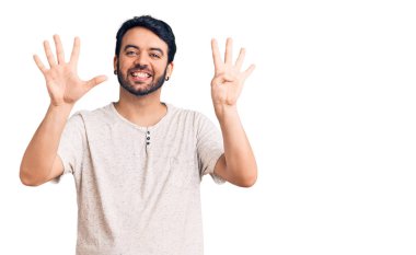 Gündelik kıyafetler giyen genç İspanyol adam dokuz numarayı gösterip işaret ederken kendinden emin ve mutlu bir şekilde gülümsüyor.. 