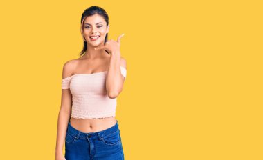 Genç, güzel bir kadın, günlük kıyafetler giyip gülümsüyor telefonla el ve parmaklarıyla jest yapıyor telefonda konuşuyor gibi. iletişim kavramları. 