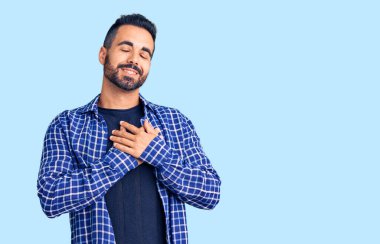 Gündelik kıyafetler giyen genç İspanyol adam elleri göğsünde, gözleri kapalı ve yüzünde minnet dolu bir jest ile gülümsüyor. sağlık kavramı. 