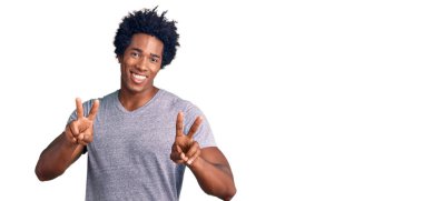 Afro saçlı, sıradan kıyafetler giyen, parmaklarını zafer işareti yaparken gösteren kameraya bakan yakışıklı Afro-Amerikalı adam. İki numara.. 