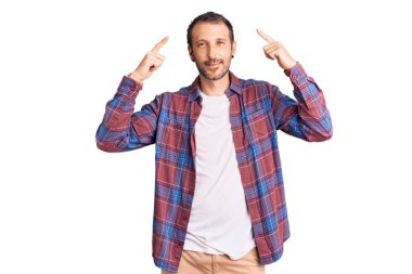 Gündelik kıyafetler giyen genç yakışıklı adam gülümseyerek iki eliyle başını işaret ediyor. Harika bir fikir ya da düşünce, iyi bir hafıza. 