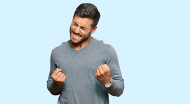 Başarılı olmak için heyecanlı, kolları havada ve gözleri kapalı, sıradan kıyafetler giyen yakışıklı İspanyol adam zaferi kutluyor. Kazanan konsept. 