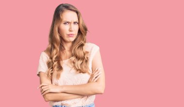 Sarışın, sıradan kıyafetler giyen, kuşkucu ve gergin genç beyaz bir kadın. Yüzünde çapraz kollarla onaylamayan bir ifade var. negatif kişi. 