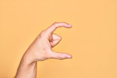 İzole edilmiş sarı arka plan üzerinde parmaklarını gösteren beyaz bir adamın eli. Görünmez bir şeyi alıp, parmaklarıyla uzayı gösteren bir nesneyi tutuyor.