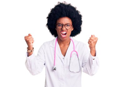 Genç Afro-Amerikalı kadın doktor önlüğü ve steteskop giyiyor kızgın ve kızgın yumruklar sallıyor öfkeyle bağırırken sinirli ve öfkeli. öfke ve agresif konsept. 