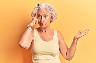 Üstün gri saçlı, günlük kıyafetler giyen, kafası karışmış ve avuç içi açık bir şekilde fotokopi alanını gösteren ve alnını işaret eden yaşlı bir kadın. Bunu bir düşün.. 