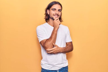 Gündelik giysiler giyen, kameraya kendinden emin, kolları çapraz ve çenesi havada gülümseyen genç yakışıklı bir adam. Olumlu düşünmek. 