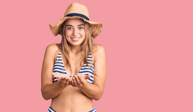 Bikini giyen ve elleri avuçlarında gülümseyen güzel sarışın kadın jest yapıyor ya da yapıyor. Bekleme ve koruma 