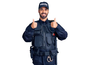 Polis üniforması giyen genç İspanyol adam elinde olumlu jest yapıyor, gülümsüyor ve mutlu. Neşeli ifade ve kazanan jest. 