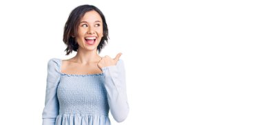 Genç ve güzel bir kız, günlük kıyafetler giyiyor, gülümsüyor, gülümsüyor ve başparmağıyla yan tarafa bakıyor.. 